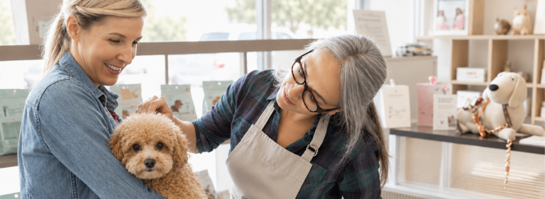 Groomer welcoming a pet parent and small dog inside a bright pet grooming salon
